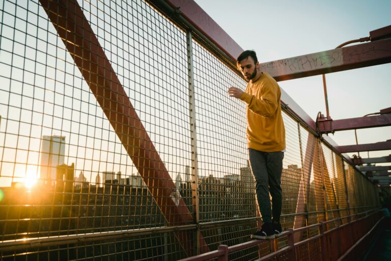 Ragazzo che cammina sulla ringhiera di un ponte di una metropoli americana al tramonto. Immagine evocativa per descrivere le azioni di rischio che i giovani commettono, senza averne la percezione. Proprio come accade quando giocano d'azzardo, non considerandone i rischi
